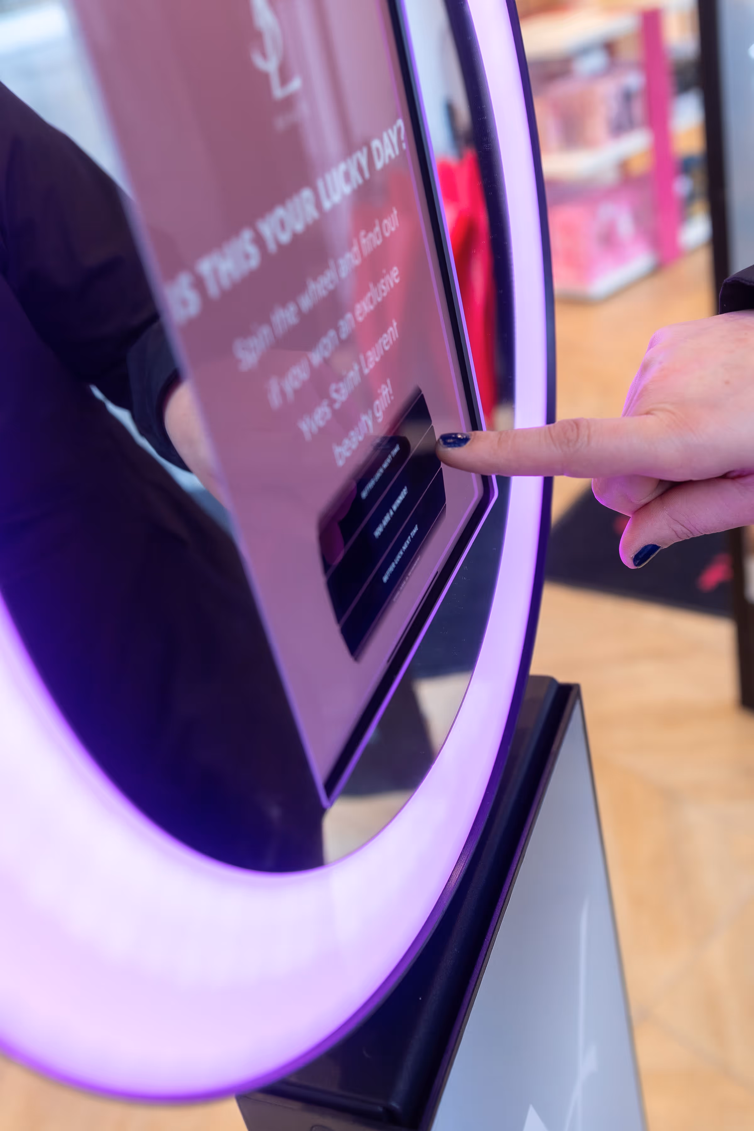 Een hand met donkerblauwe nagellak die een knop op een roze interactief scherm met paarse verlichting indrukt.