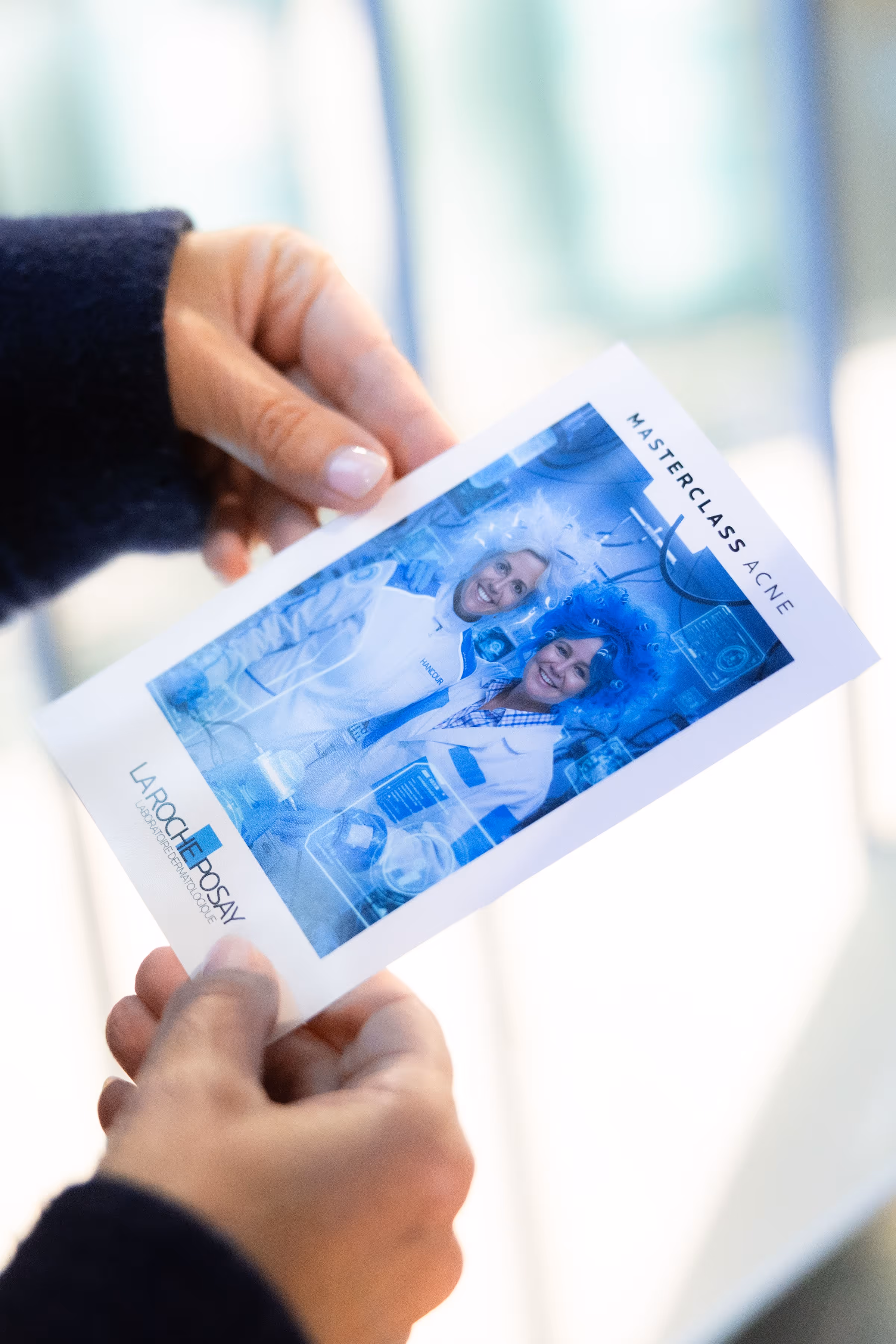 Twee lachende vrouwen in witte laboratoriumjassen dragen blauwe en witte pruiken op een foto met tekst Masterclass Acne en La Roche-Posay logo.