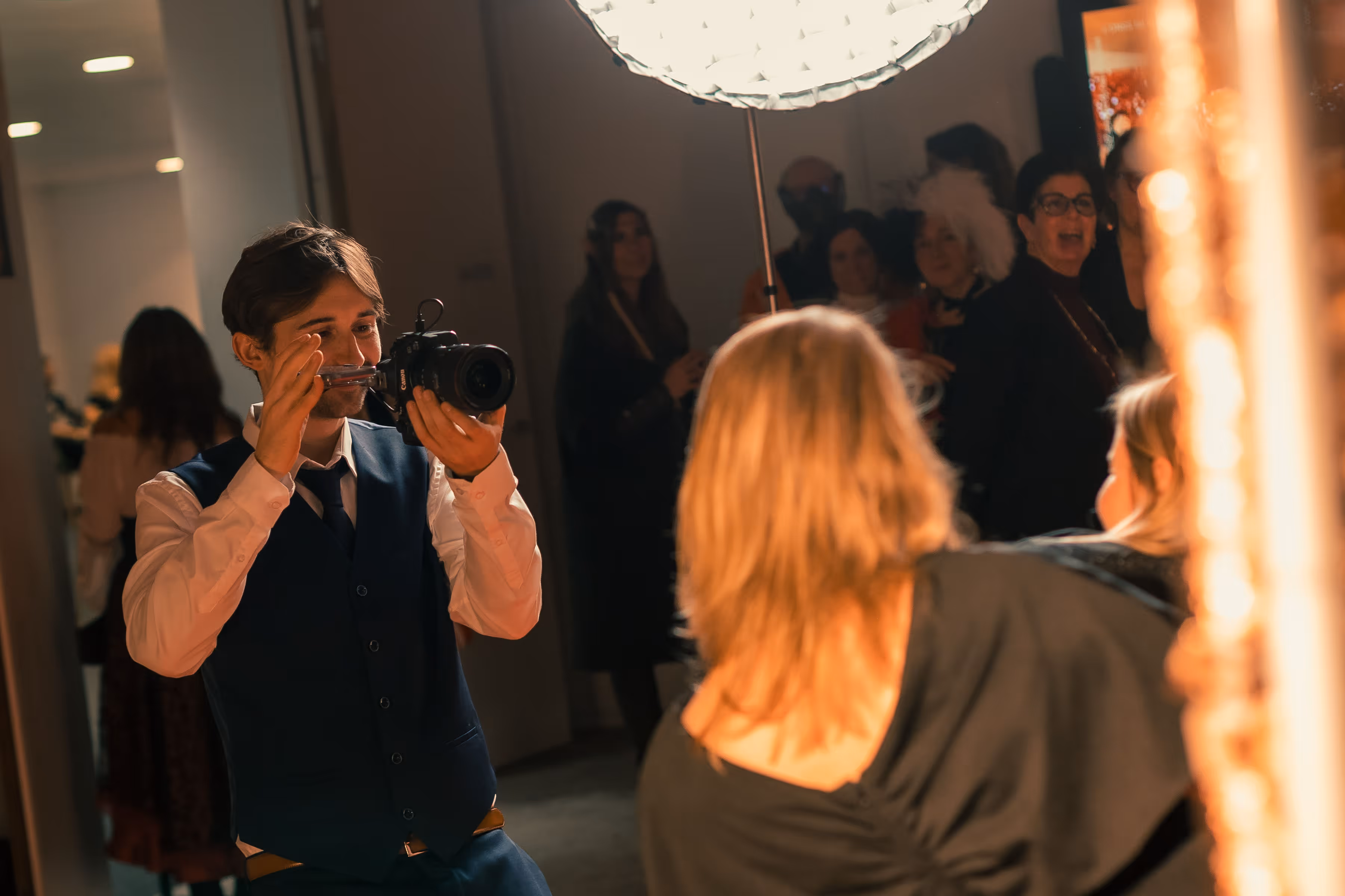 Man met een camera neemt een foto van een vrouw met blond haar op een evenement met een groep mensen op de achtergrond.
