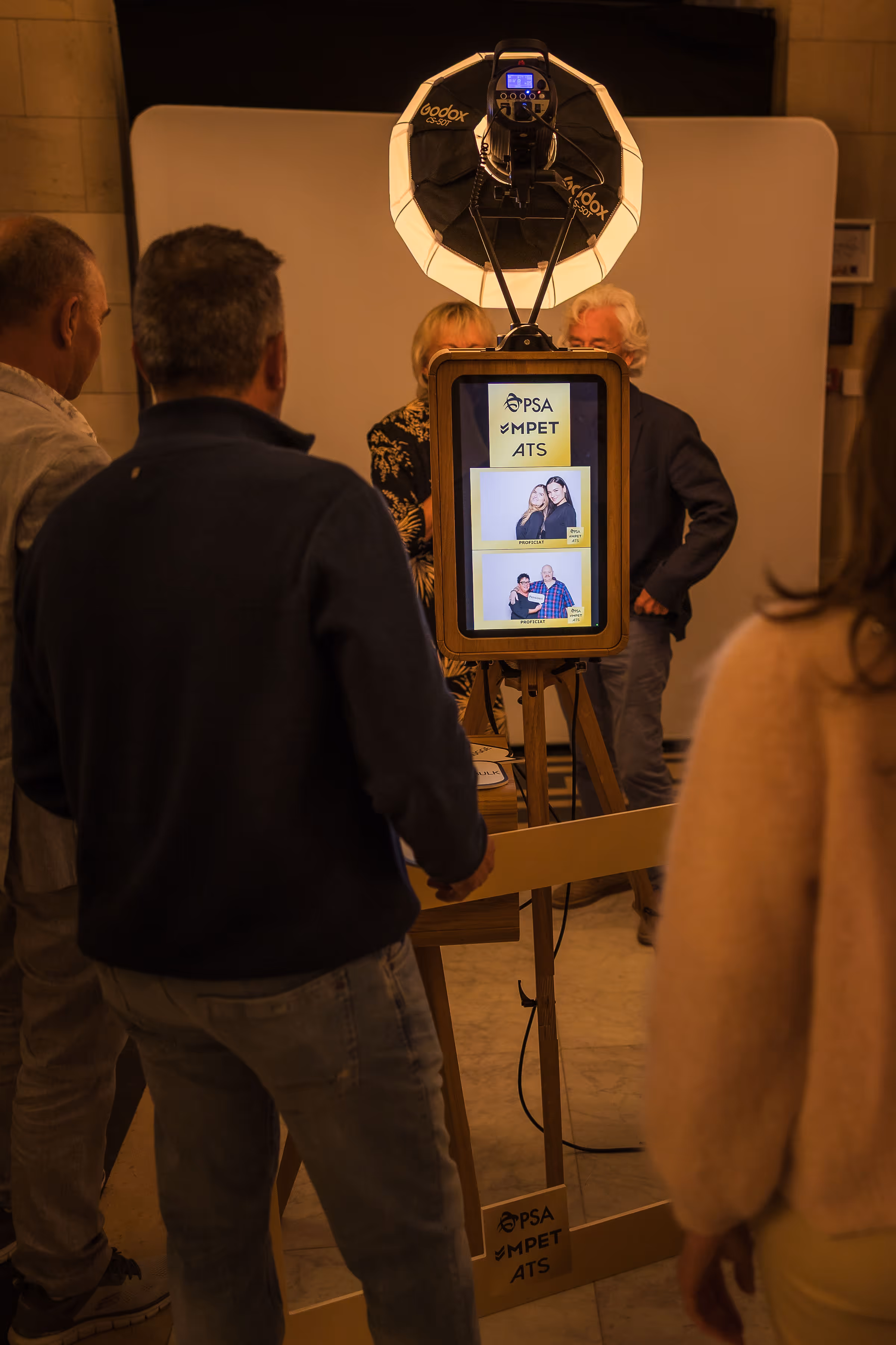 Groep mensen staat rond een fotoshootapparaat met digitale display waarop twee foto’s van mensen te zien zijn met de tekst PSA MPET ATS.