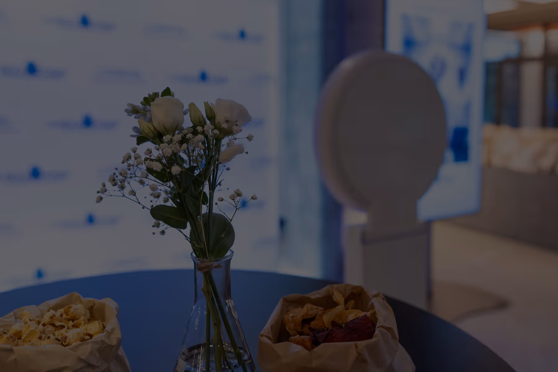 Een vaas met witte bloemen op een tafel, omringd door zakjes met gekruide snacks.