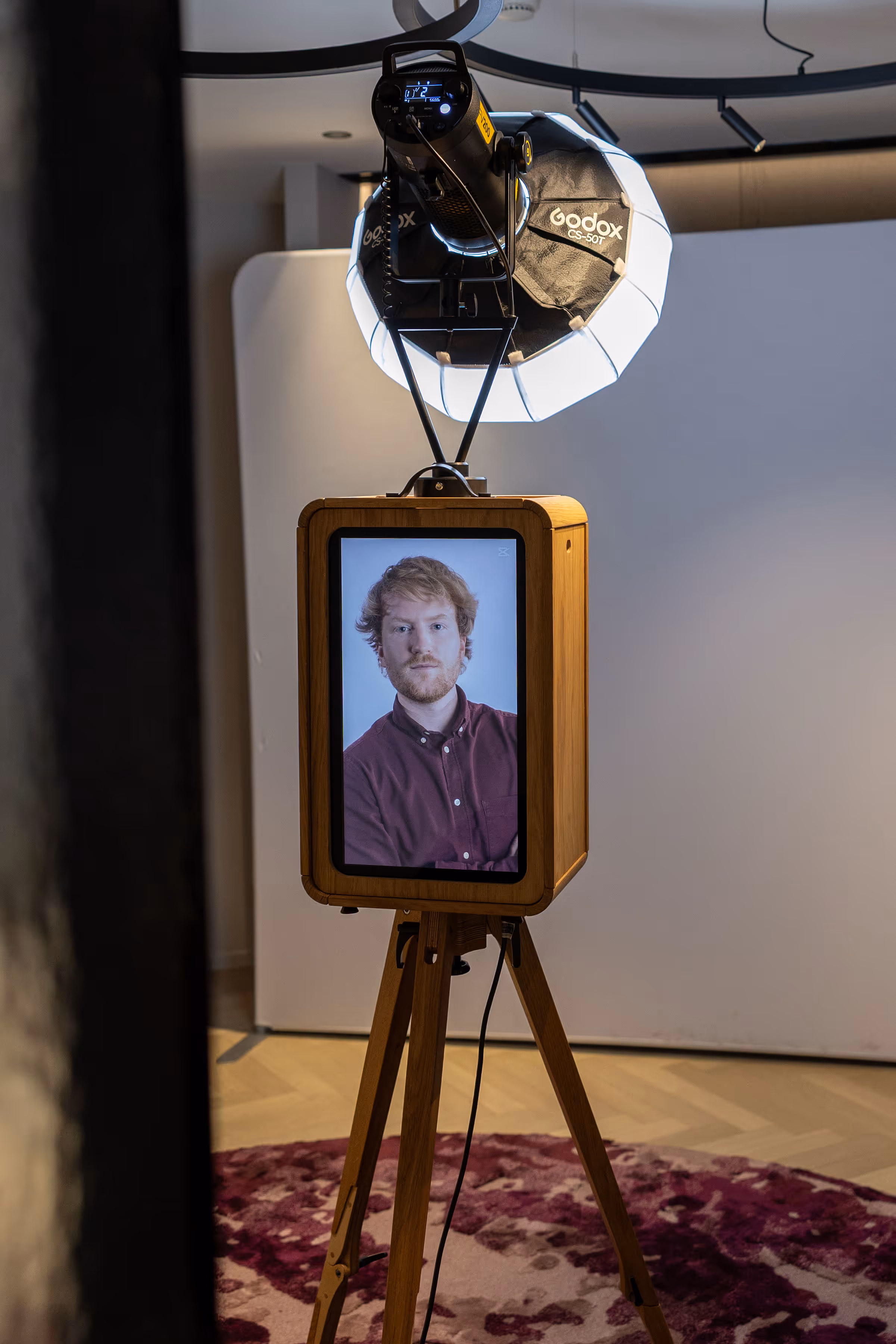 Een houten kast op een statief met een scherm dat het portret toont van een man met rood haar en een roodbruin hemd, verlicht door een Godox CS-50T studiolamp.