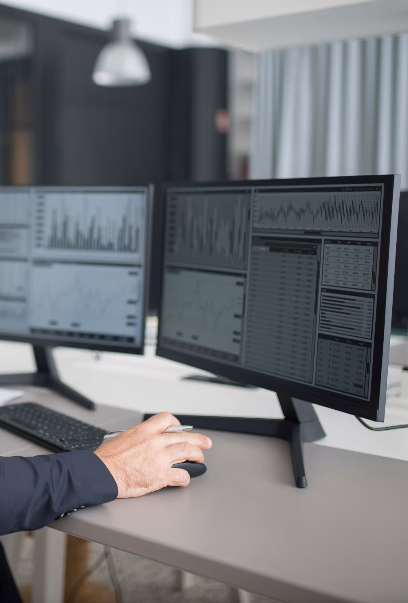 Hand bedient eine Computermaus vor zwei Monitoren mit Daten.