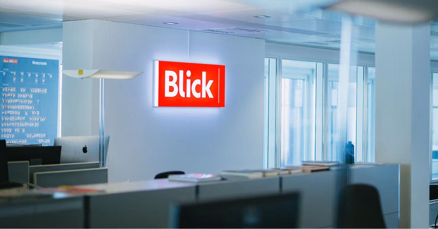 Innenansicht eines modernen Büros mit rotem Blick-Logo an der Wand und Schreibtischen.