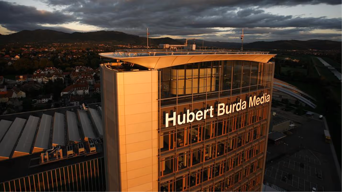 Hochhaus mit der Aufschrift Hubert Burda Media im warmen Abendlicht, Stadt und Berge im Hintergrund.
