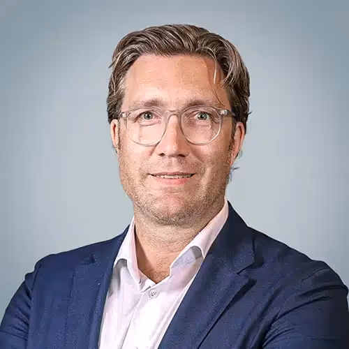 Porträt eines Mannes mit Brille, weißen Hemd und blauem Sakko vor hellem Hintergrund.