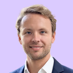 Porträt eines lächelnden Mannes mit kurzen blonden Haaren vor lila Hintergrund.