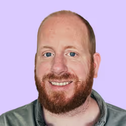 Lächelnder Mann mit rotem Bart und kurzem Haar vor lila Hintergrund.