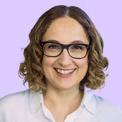 Fröhliche Frau mit kurzen lockigen Haaren, Brille und weißer Bluse vor lila Hintergrund.