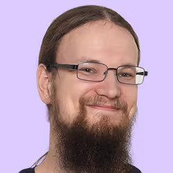 Lächelnder Mann mit langem Bart, Brille und zurückgebundenem Haar vor lila Hintergrund.