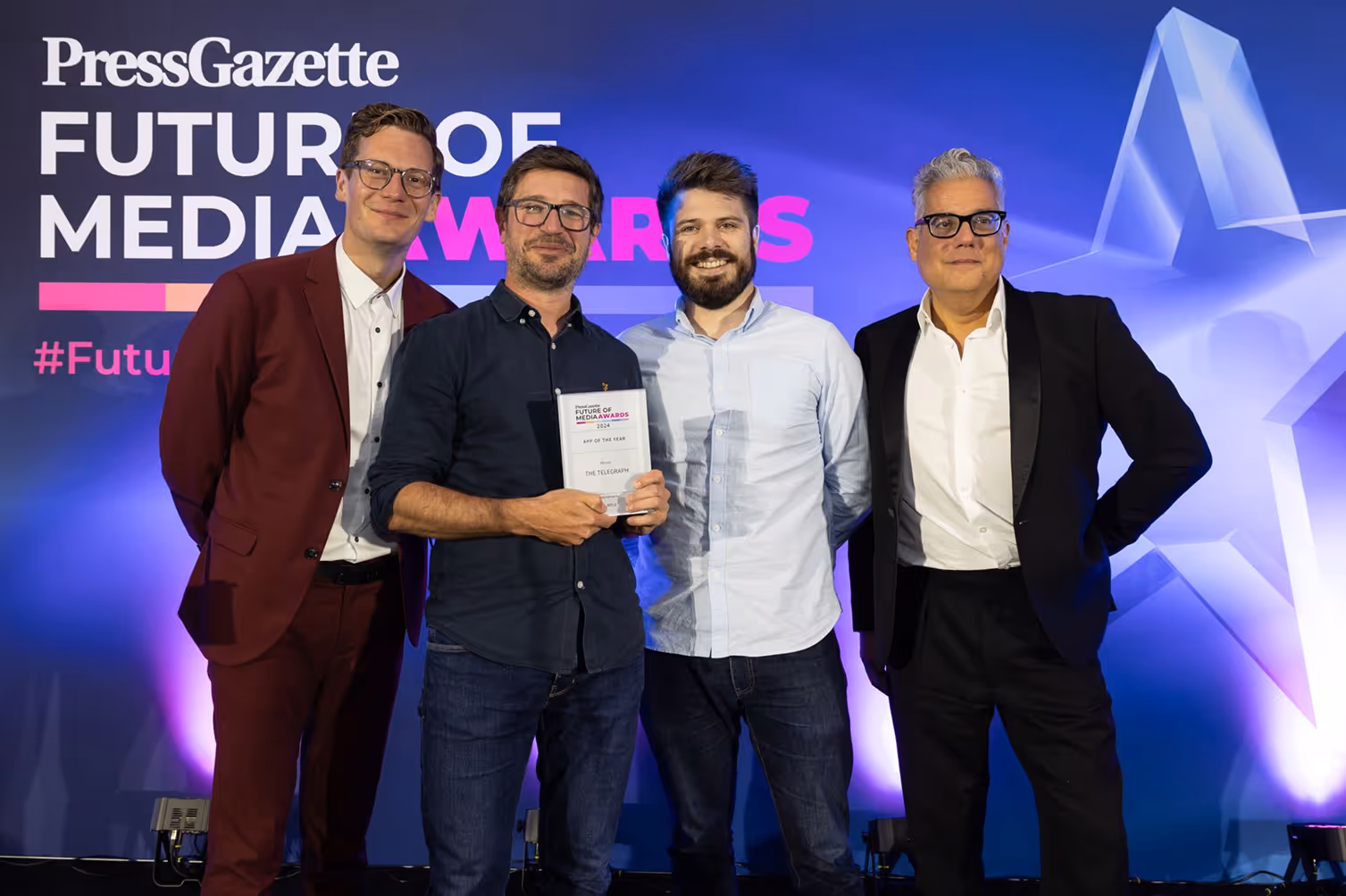 Vier Männer bei den Future of Media Awards vor lila-blauem Hintergrund, einer hält eine Auszeichnung.