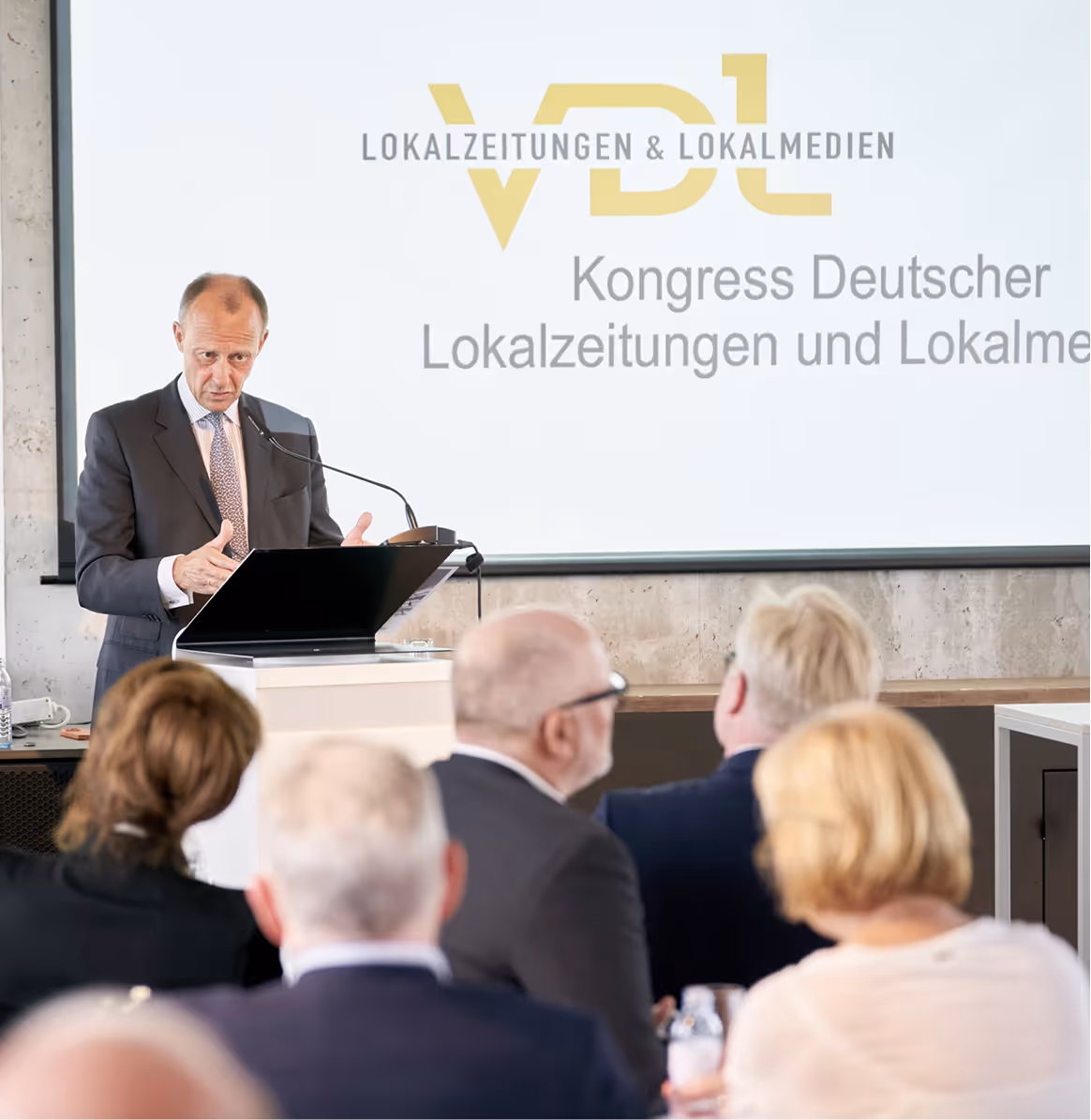 Mann hält Vortrag am Podium auf Kongress für deutsche Lokalzeitungen vor Publikum.