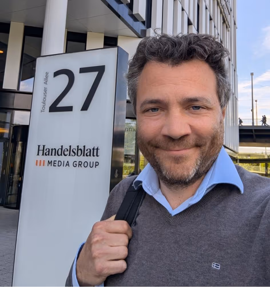 Mann mit Bart vor Schild der Handelsblatt Media Group auf Toulouser Allee 27.