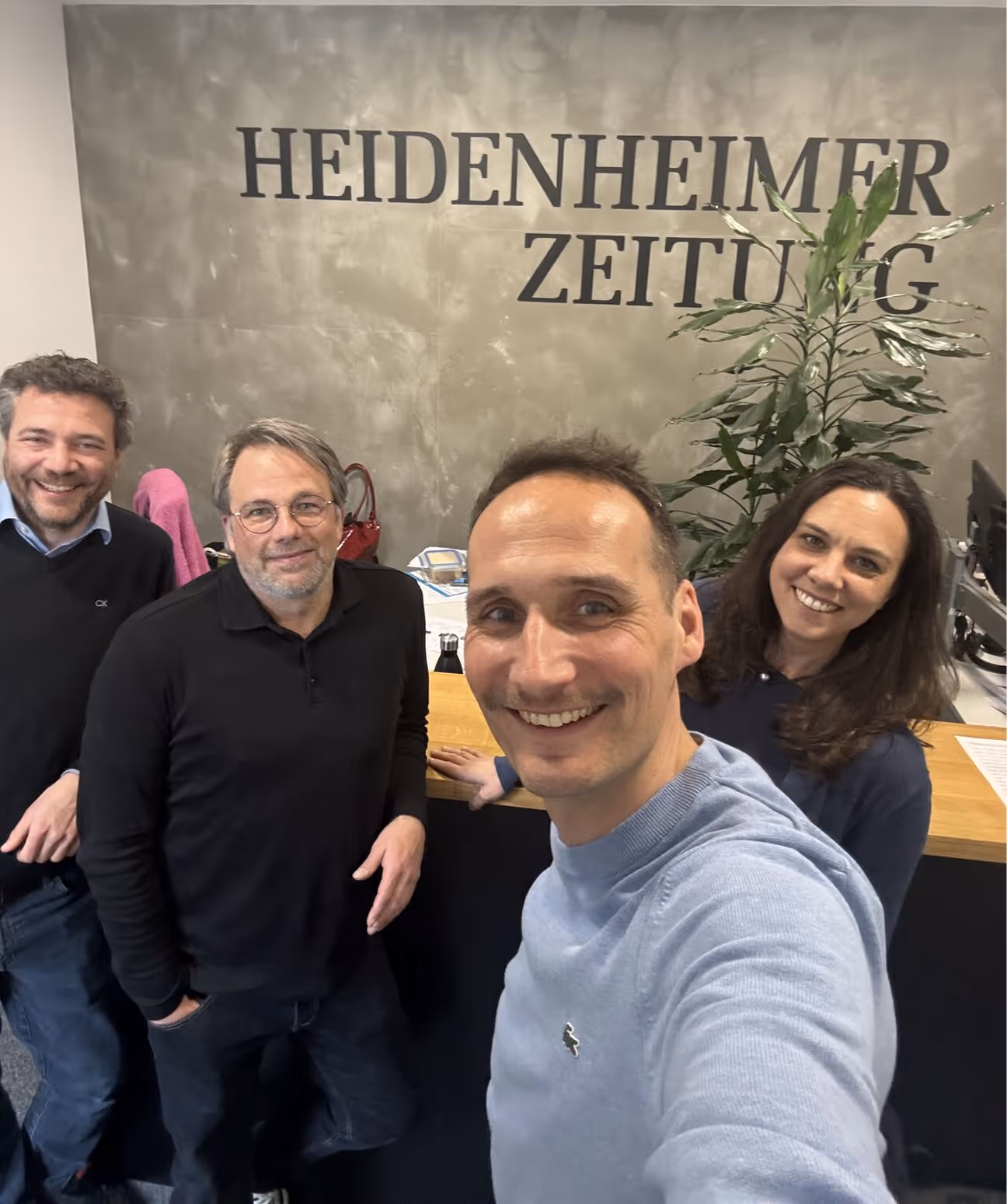 Vier lächelnde Personen vor einer Wand mit dem Schriftzug Heidenheimer Zeitung.