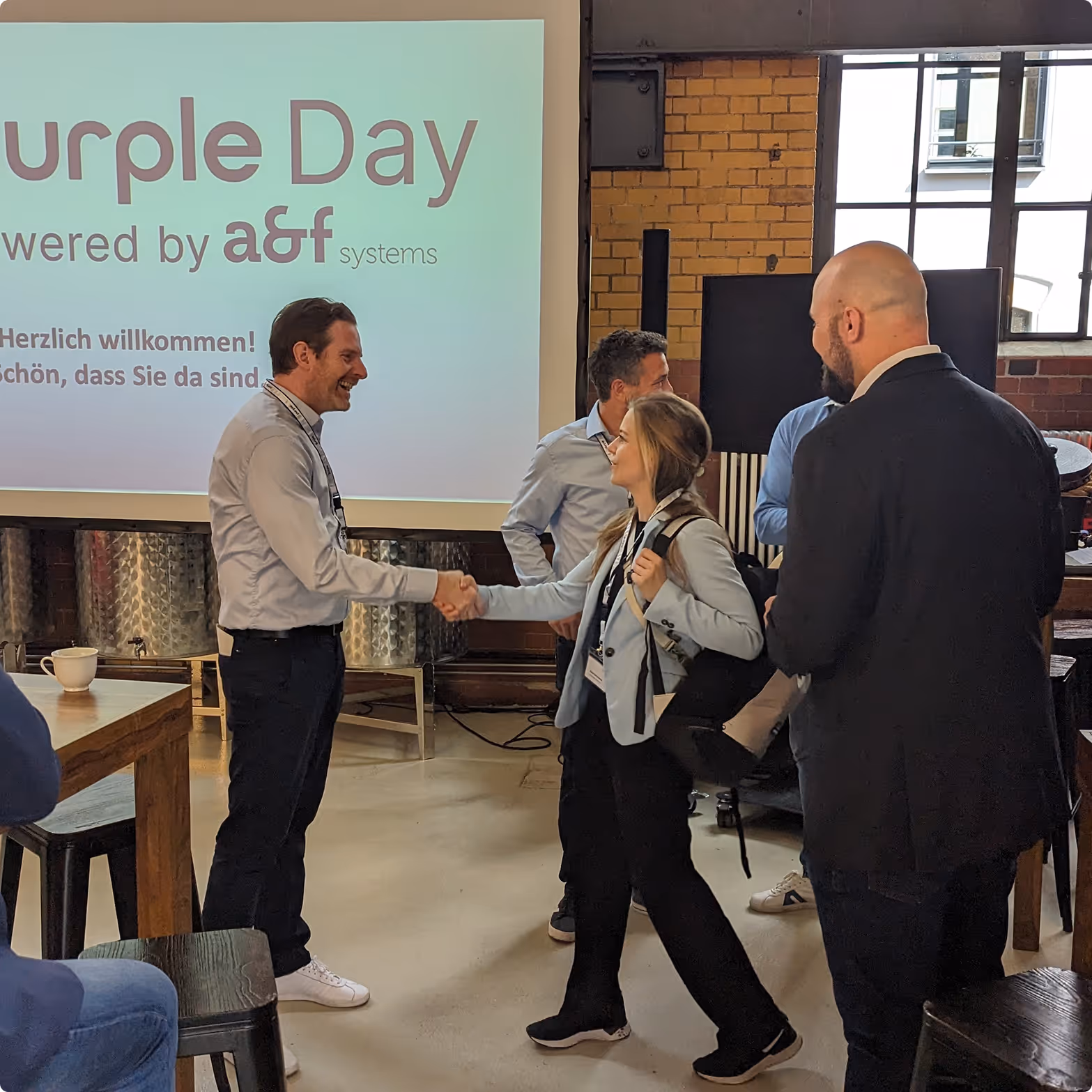 Zwei Personen geben sich bei einem Event mit 'Purple Day' Begrüßung die Hand.