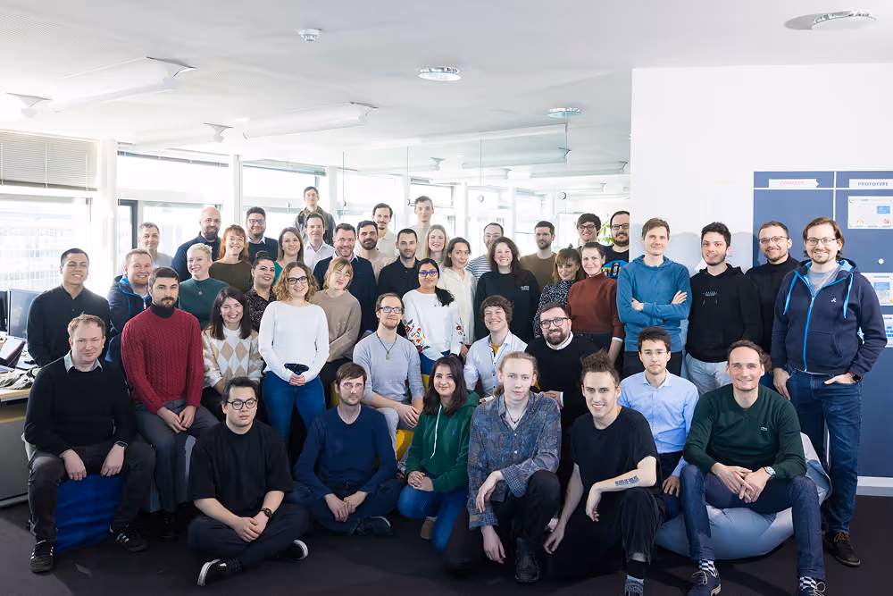 Gruppenfoto von 40 Personen in einem Büro mit Fenstern und moderner Beleuchtung.