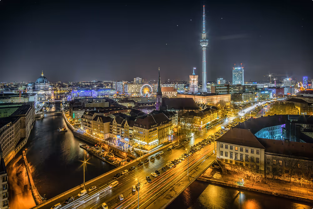 Nächtliche Stadtansicht mit beleuchteten Straßen, Gebäuden und Fernsehturm in der Ferne.