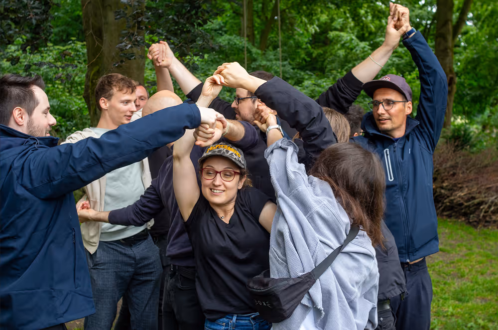 Gruppe von Menschen im Freien, die sich an den Händen halten und zusammen ein Spiel oder Teamaktivität machen.