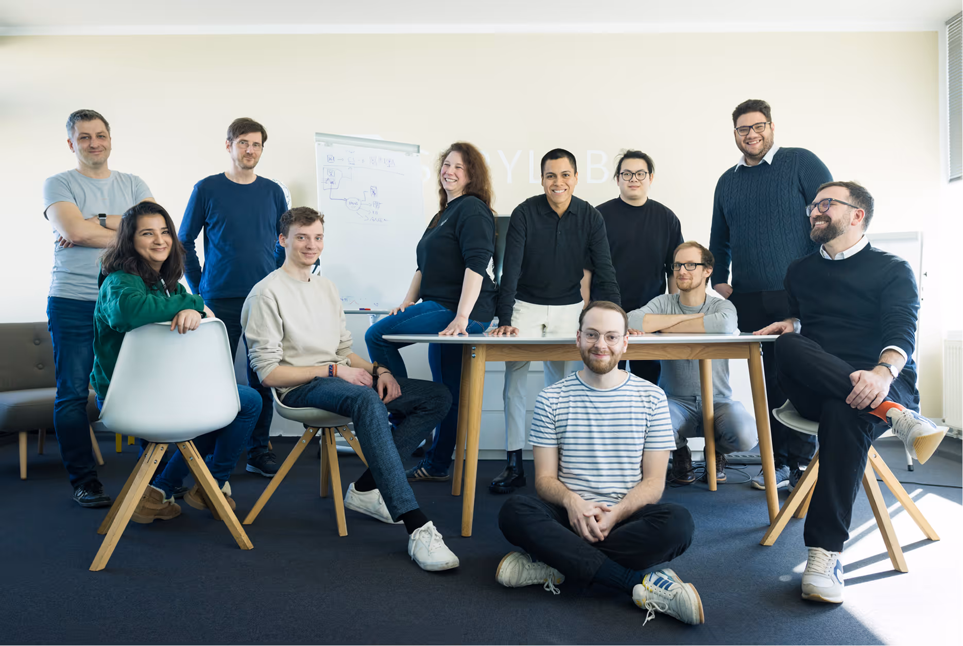 Gruppenfoto von elf Personen im Büro, lächelnd, einige sitzen, andere stehen um einen Tisch herum.