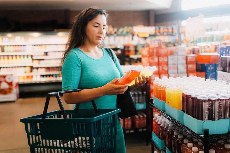 A woman standing in a grocery store while comparing drinks.