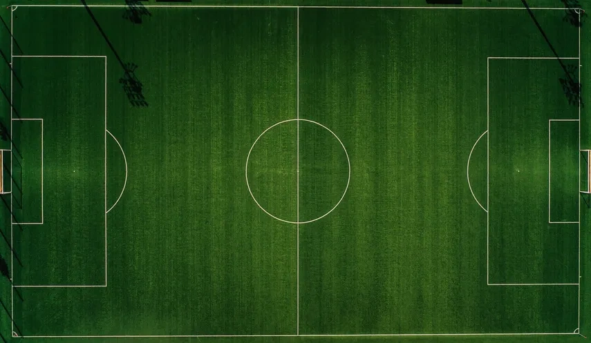 Aerial view of an empty green soccer field with white boundary lines and goals.