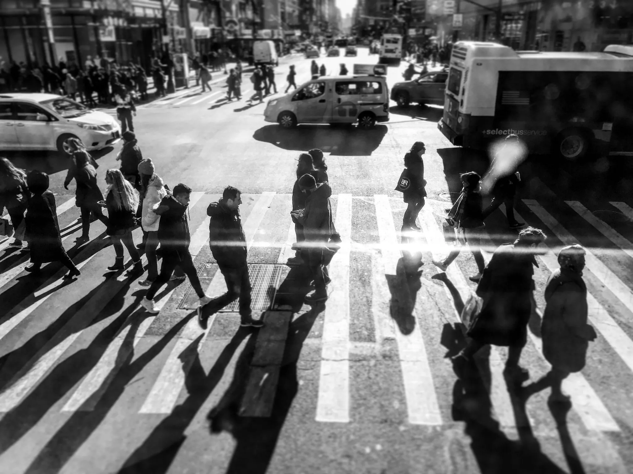     Black-and-white street scene of pedestrians crossing a busy New York City intersection.