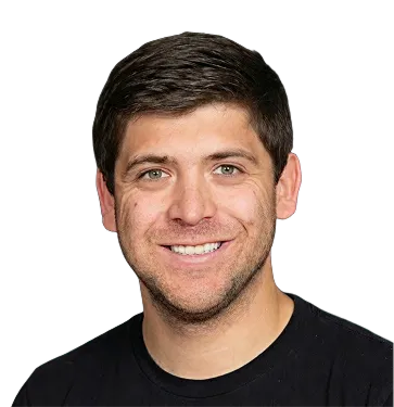 Smiling man with short dark hair and light facial stubble wearing a black shirt, shown on a transparent background.