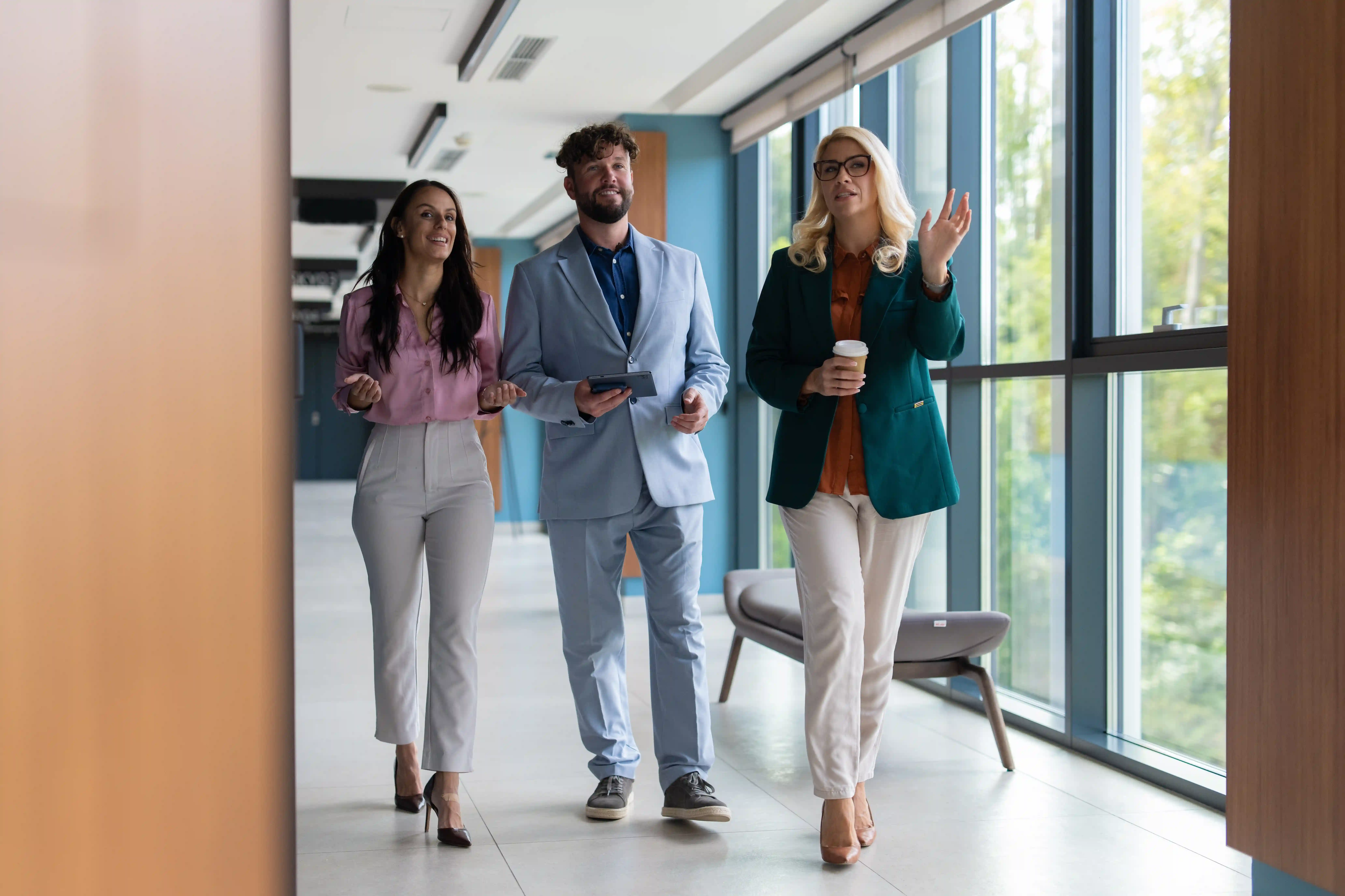 Three corporate colleagues discussing strategy while walking in an office, representing the multi-stakeholder buying committees unique to enterprise B2B marketing.