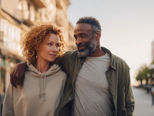 Smiling couple walking outdoors with arms around each other at sunset.
