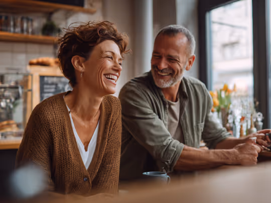 Smiling middle-aged couple enjoying coffee and laughter in a cozy cafe.