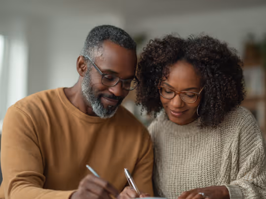 Smiling couple wearing glasses signing papers together indoors.