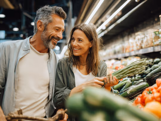 Smiling couple shopping for fresh vegetables in a grocery store produce aisle.