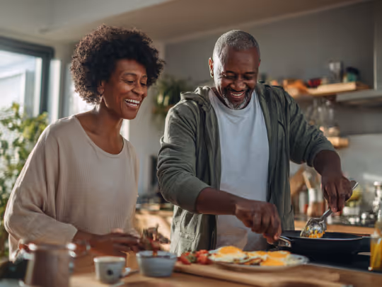 Smiling man and woman cooking breakfast together in a bright modern kitchen.