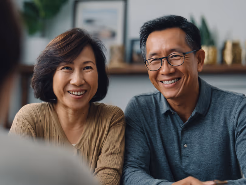 Smiling middle-aged Asian couple listening attentively in a cozy home setting.
