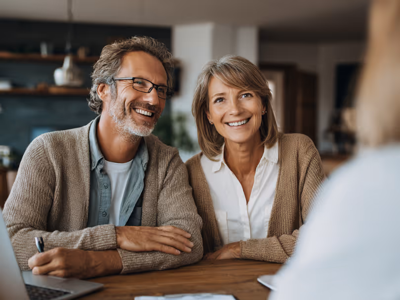 Smiling middle-aged couple sitting at a table during a meeting with a person across from them.