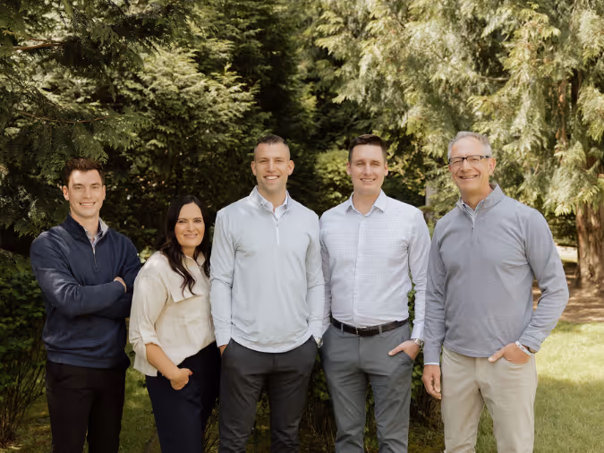 The Gevers Wealth team, standing outdoors in front of trees smiling at the camera.