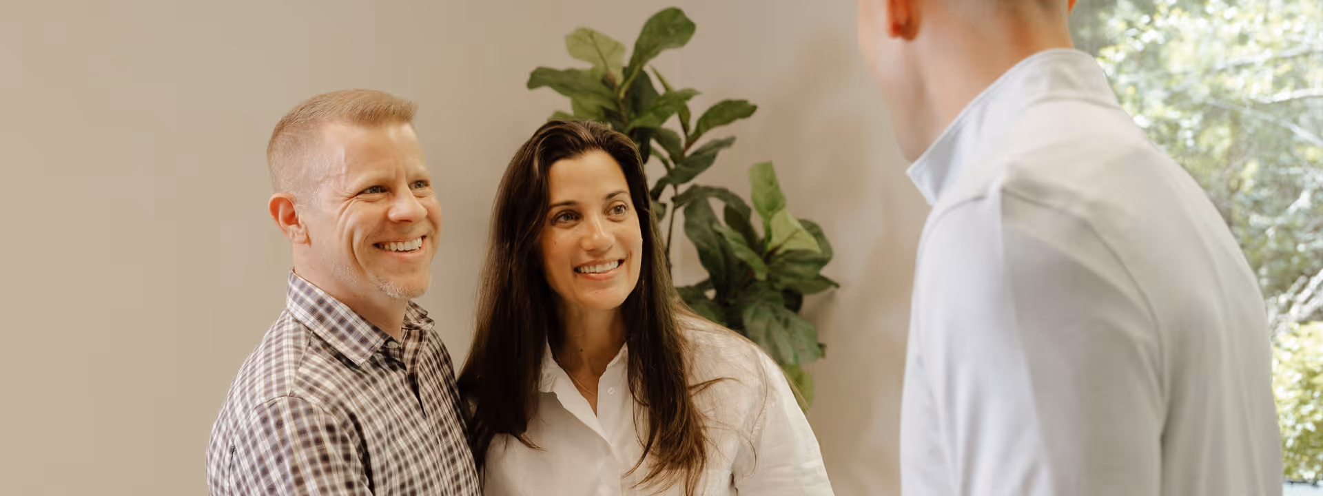 Smiling couple shaking hands with a financial advisor in a light office with plant decor.
