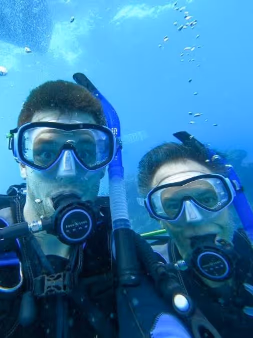 Two scuba divers underwater wearing masks and regulators with bubbles rising around them.