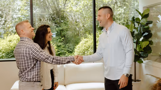 Trey Gevers shaking hands with a couple in a bright room with large windows and plants.