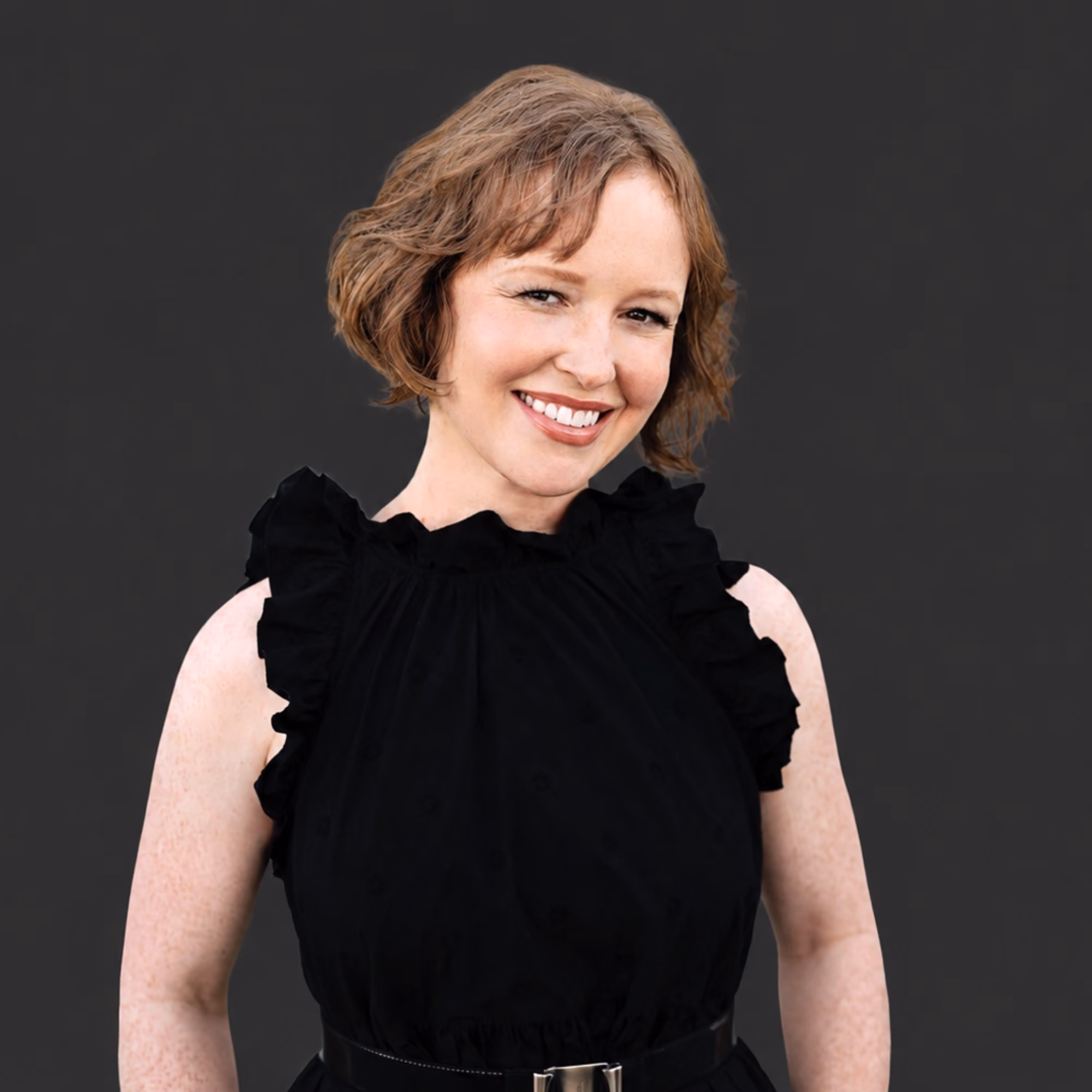 Professional headshot of Kristin Van Ausdal Senior Principal at MMC, a woman with shoulder-length dark brown hair wearing a dark top and a delicate necklace, smiling against a dark background.