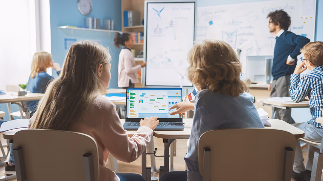 Two children sitting in class using a touchscreen to learn.