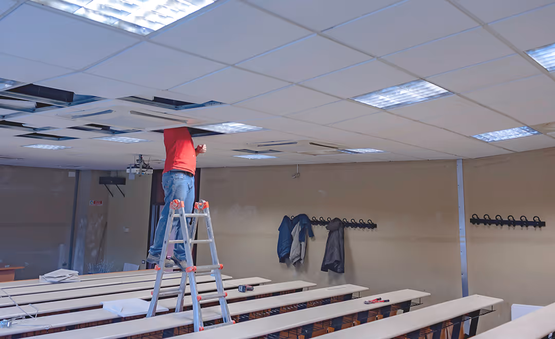 A man on a ladder working on a classroom ceiling.