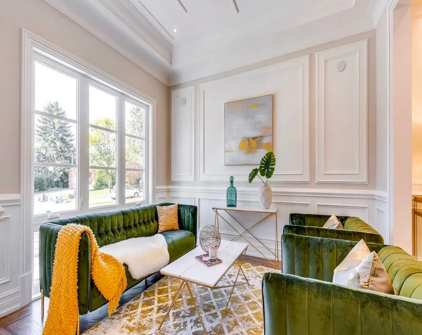 Bright living room with green velvet sofas, yellow throw blanket, white rug, marble coffee table, and wall art.