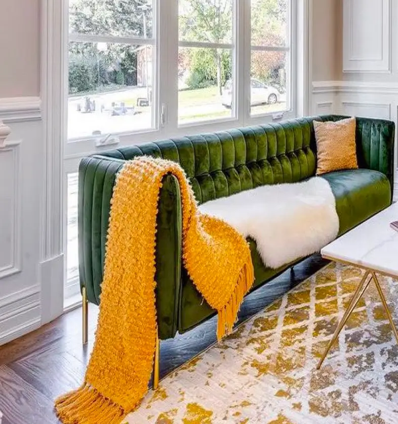 Green velvet sofa with a yellow throw and pillow in a bright living room near large windows.