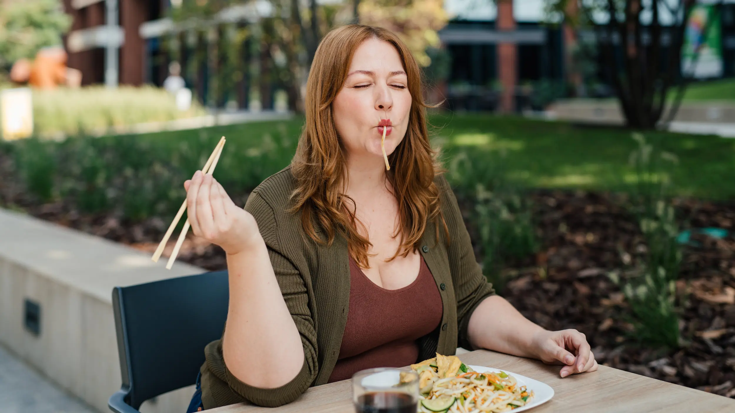 Mid sized woman happily eating noodles