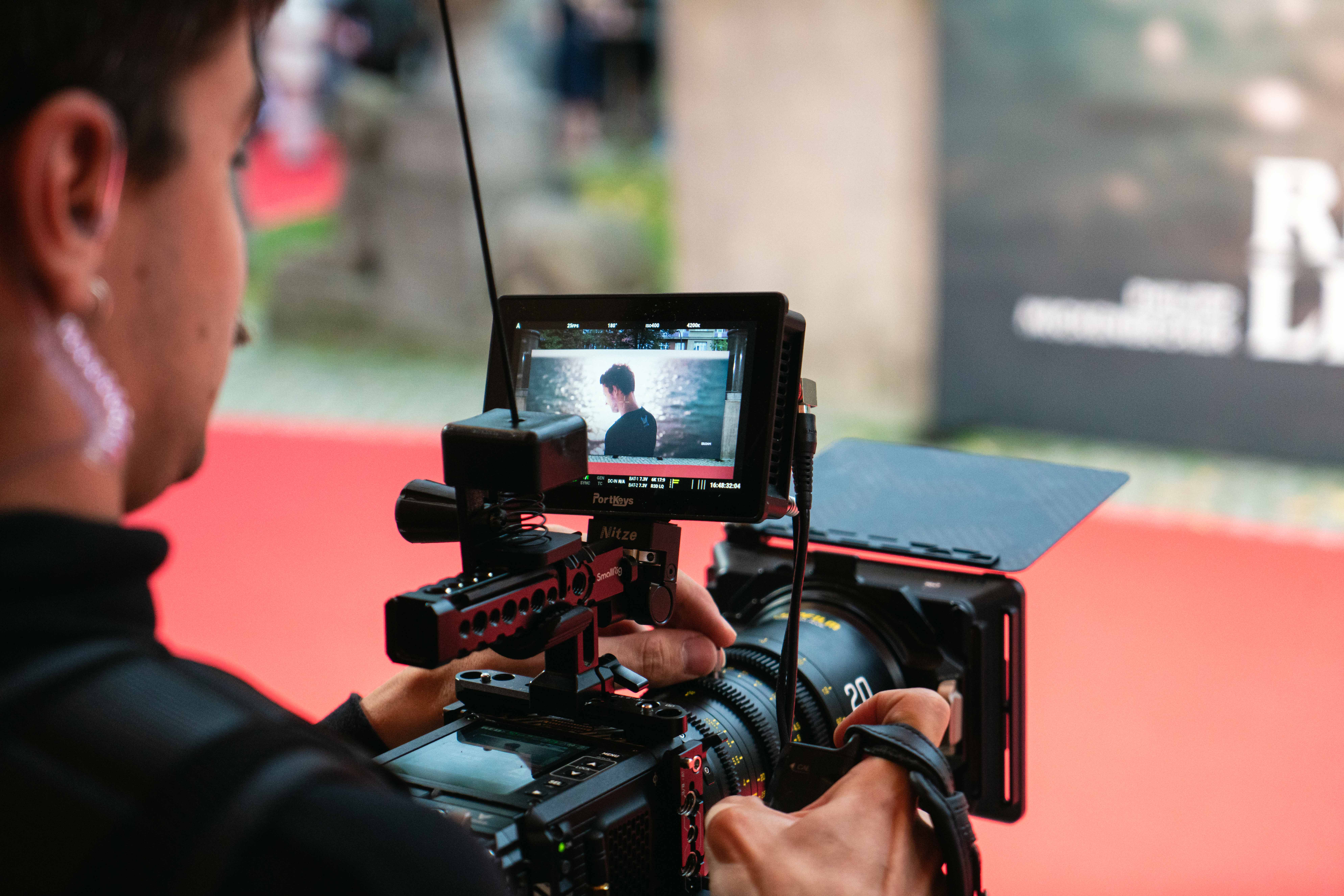 Videographer filming a man near water, visible on the camera monitor.