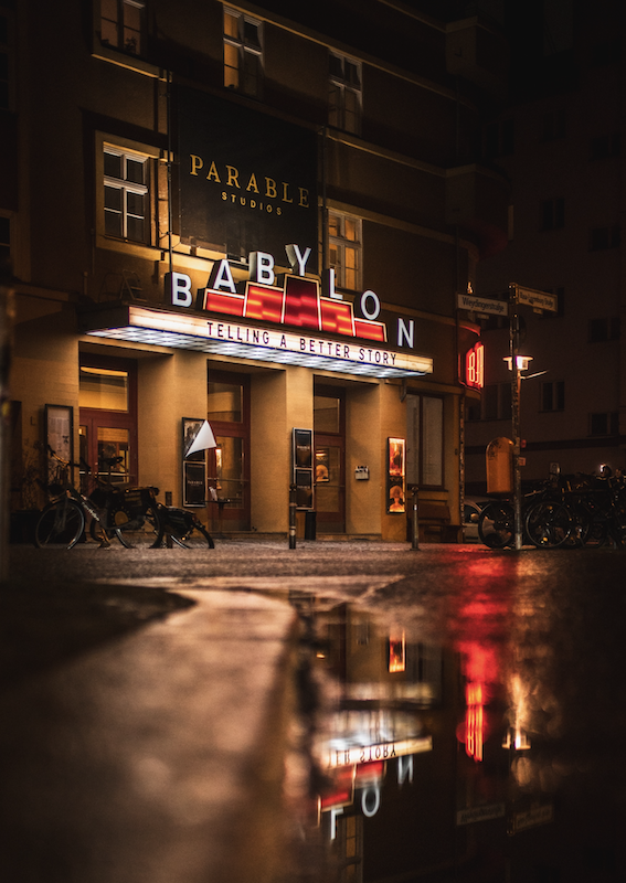 Night view of Babylon cinema entrance with illuminated sign and wet pavement reflecting the lights.