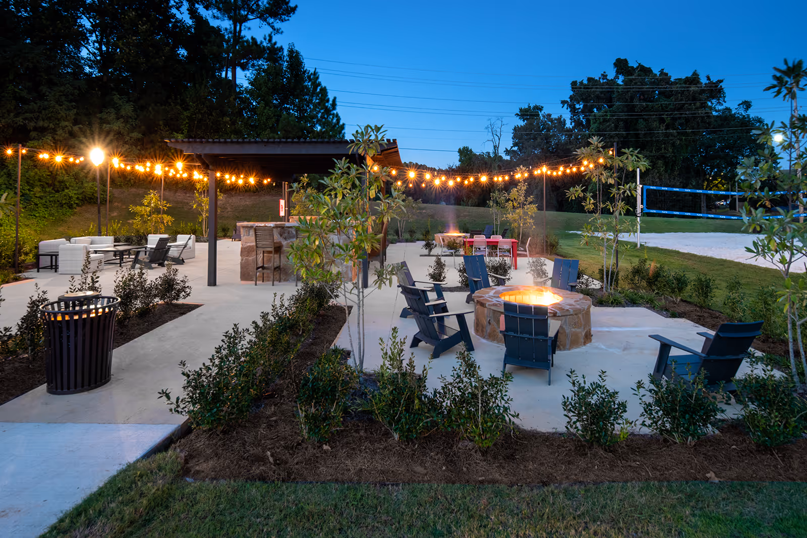 Fire pit area with lit fire pit, chairs, and hanging lights