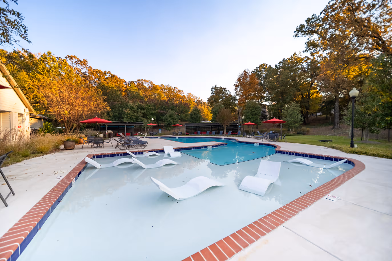 Wide view of Swimming pool with lounge chairs and tables and chairs with umbrellas