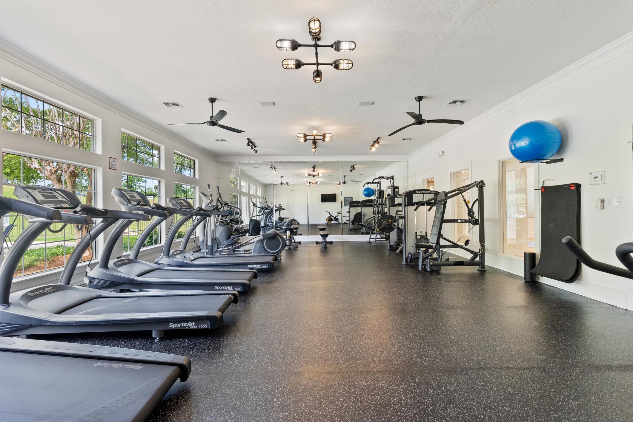 Gym featuring treadmills, full mirrored wall, and large windows
